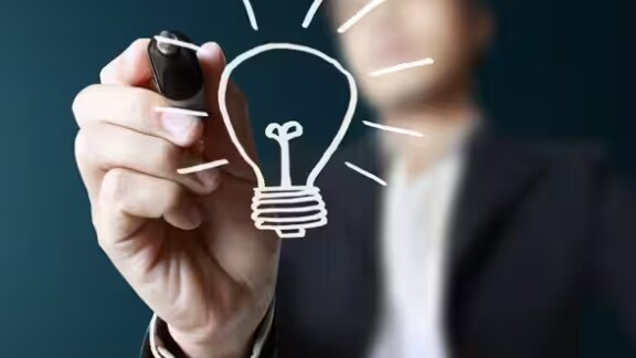 Man drawing a lightbulb on glass surface
